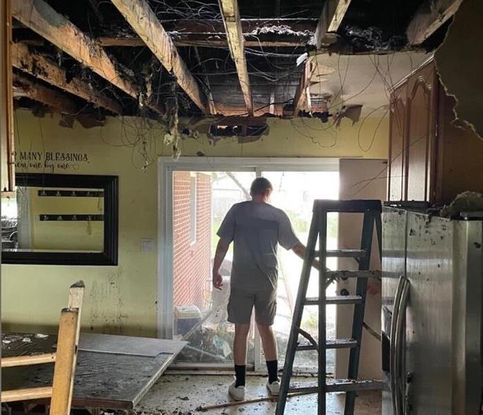 man in grey shirt standing in fire-damaged dining room